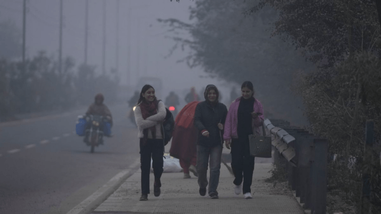 Commuters and vehicles moving through dense winter fog in Delhi‑NCR affecting visibility.