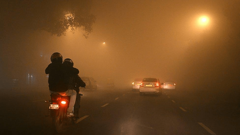 Cars driving with headlights on through dense fog reducing visibility on North Indian roads.