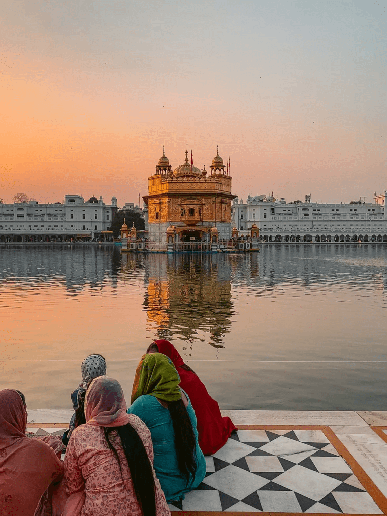 Golden Temple at sunrise with Sikh devotees reflecting by the sarovar